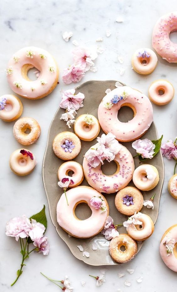 Selection of different sized pastel pink and white donuts with flowers on them - 14 Bridgerton hen party ideas - party food  - Floral sweet treats