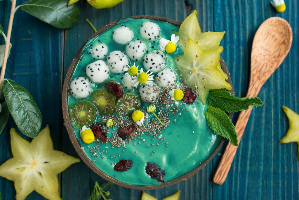 A Bowl full of blue creamy substance topped with various exotic fruits