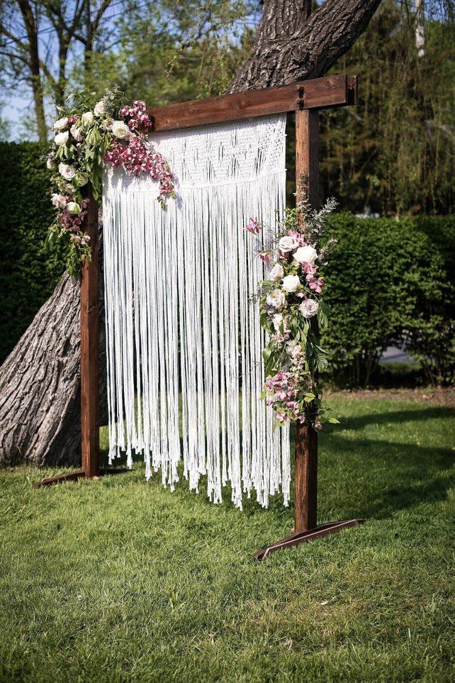 A Wedding alter made of wood white white macrame rope hanging from it 