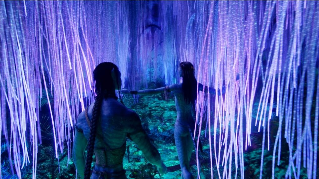 A still frmo the avatar movie of two characters walking through the hanging purple branches of the tree of souls and touching them. They are glowing and the floor of the forest is a glowing blue green